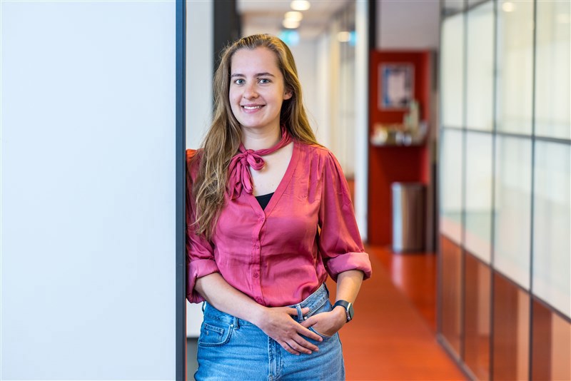 Een vrouwelijke medewerker leunt tegen muurt en kijkt in de camera