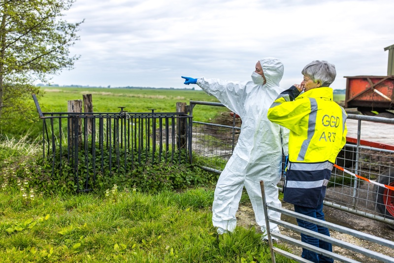 Een forensisch arts staat in een weiland en overlegt met een medewerker in een wit pak